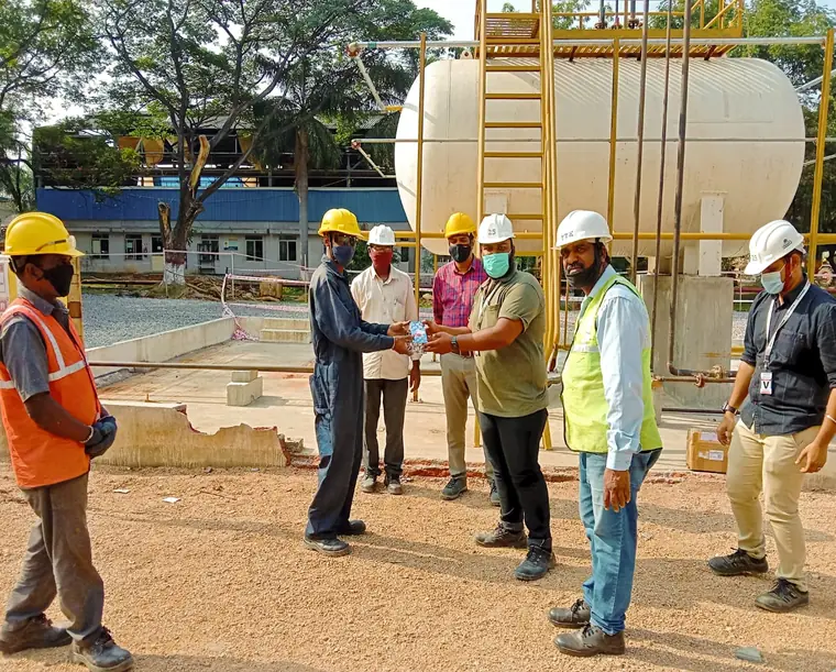HSE team in hard hats and hi-vis briefing beside a storage tank on an outdoor site